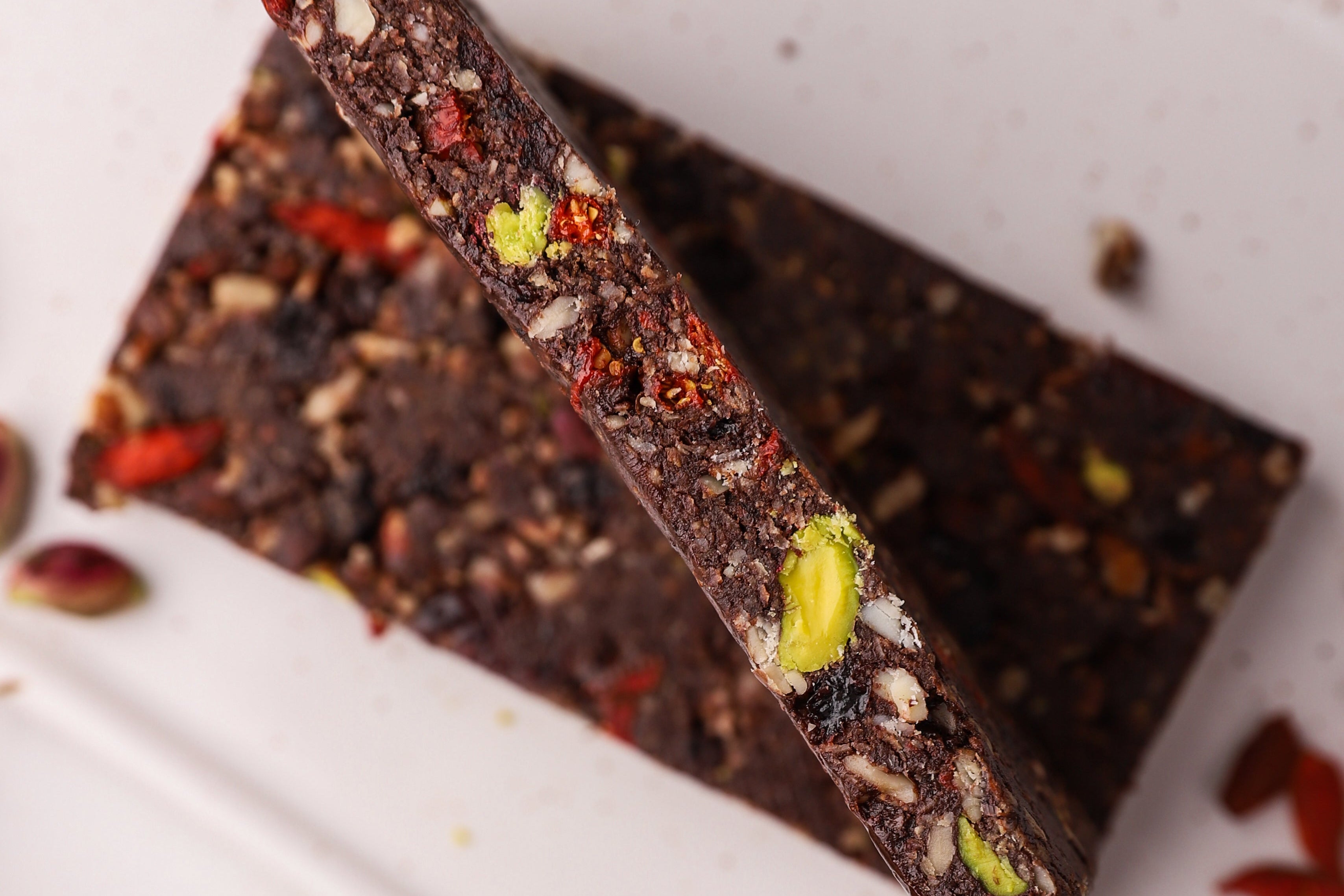 Cocoa and cranberries raw energy bar with pistachios and goji berries on a white surface